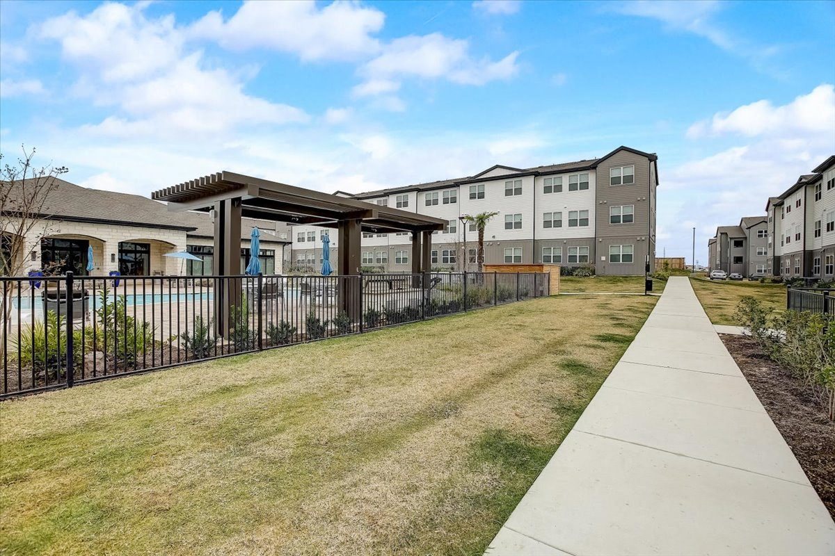 Walking path along the pool courtyard with shaded pergola structure and maintained open lawn.